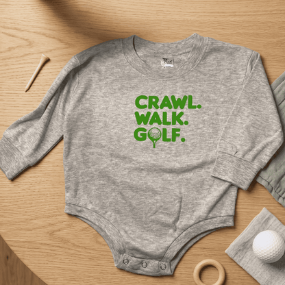 Gray baby onesie with 'CRAWL. WALK. GOLF.' text on a wooden surface with golf-themed items.