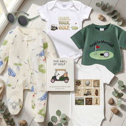 Collection of children's clothing and a book titled 'The ABCs of Golf' on a light wooden surface with greenery.