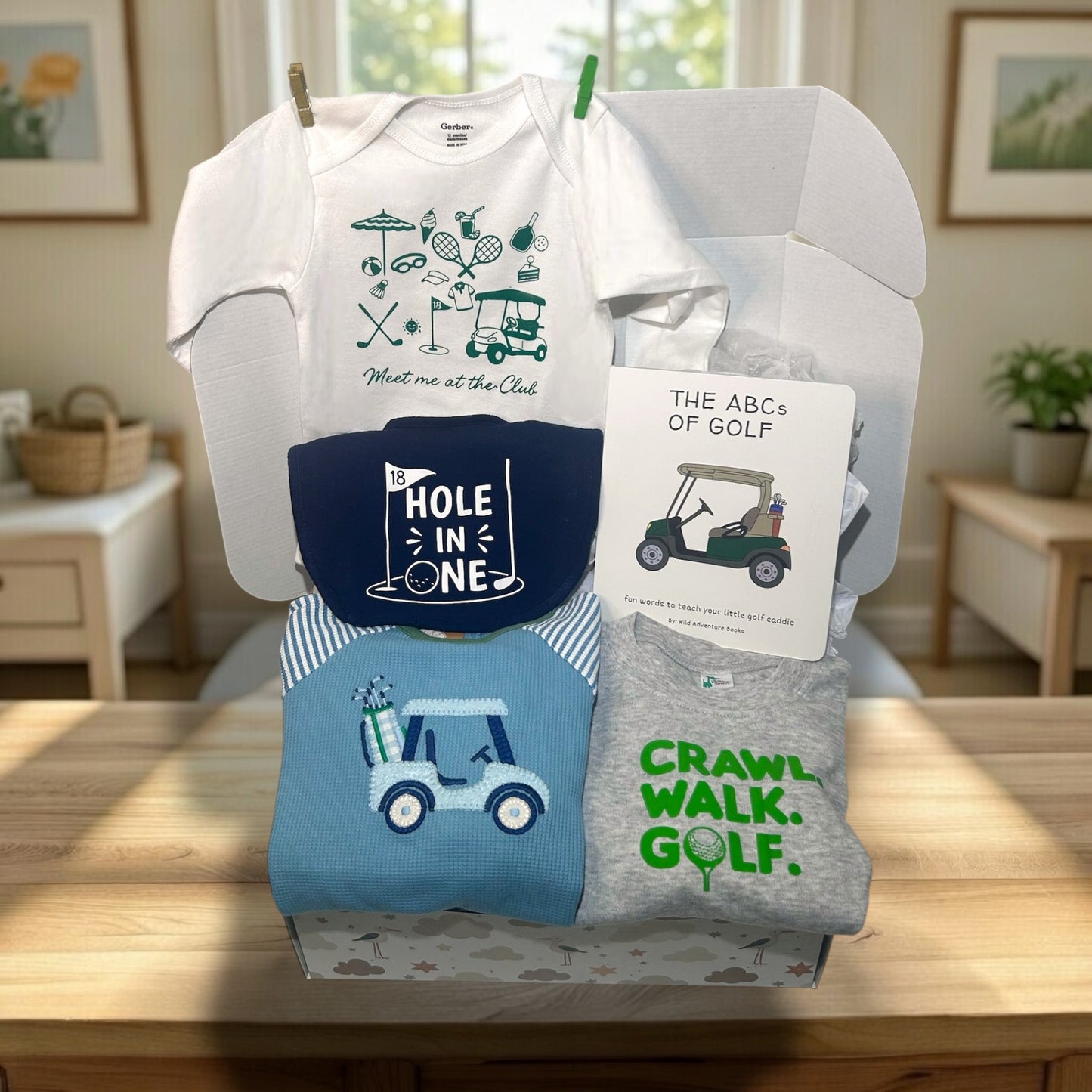 Collection of baby clothing and accessories with golf-themed designs on a wooden surface.