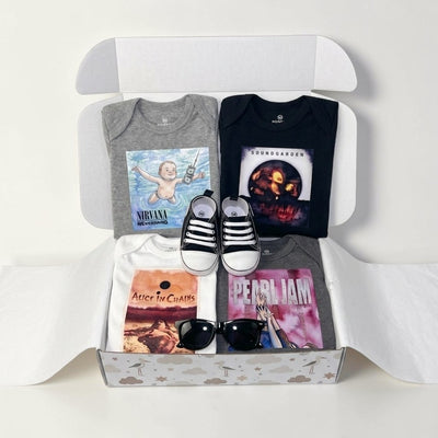 A curated gift box set containing a gray Nirvana band t-shirt, a black Korn band t-shirt, a white Alice in Chains t-shirt, and a gray Pearl Jam t-shirt, styled with black and white sneakers, sunglasses, and a white box on a white background.