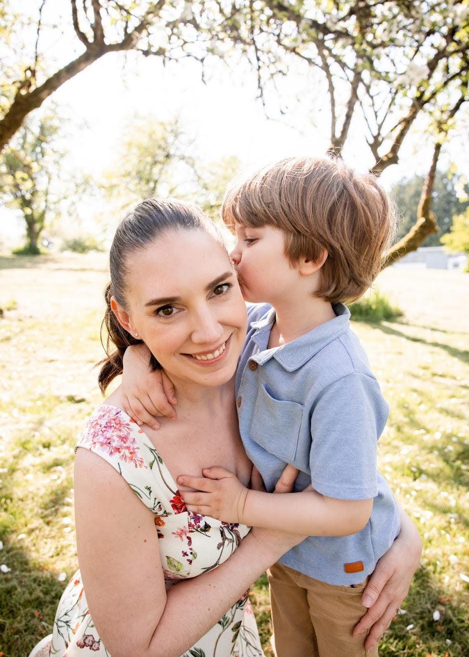 Woman holding a child in a park with trees and sunlight