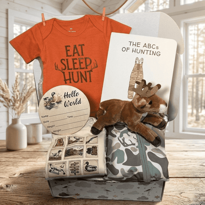 Baby gift set with orange 'Eat Sleep Hunt' shirt, book, and plush toy on a wooden surface.