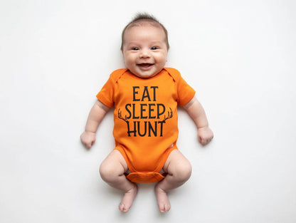 Baby wearing an orange onesie with 'EAT SLEEP HUNT' text on a white background