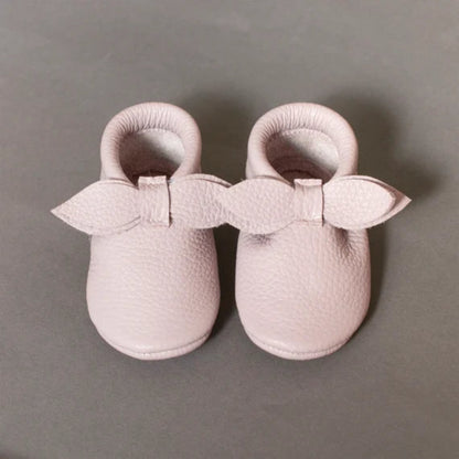 Pair of pink baby shoes with bows on a gray background