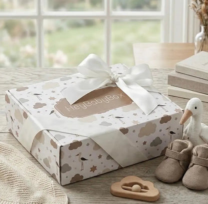 Baby gift set with 'Hey Baby Box' box, shoes, and toys on a wooden surface.