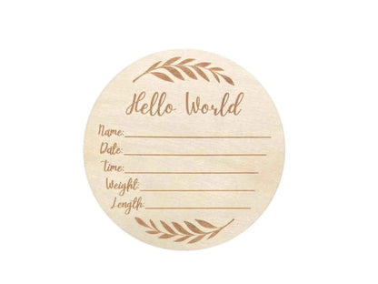 Round wooden baby milestone plaque with 'Hello World' engraving, leaf design, and fill-in fields for name, date, time, weight, length.