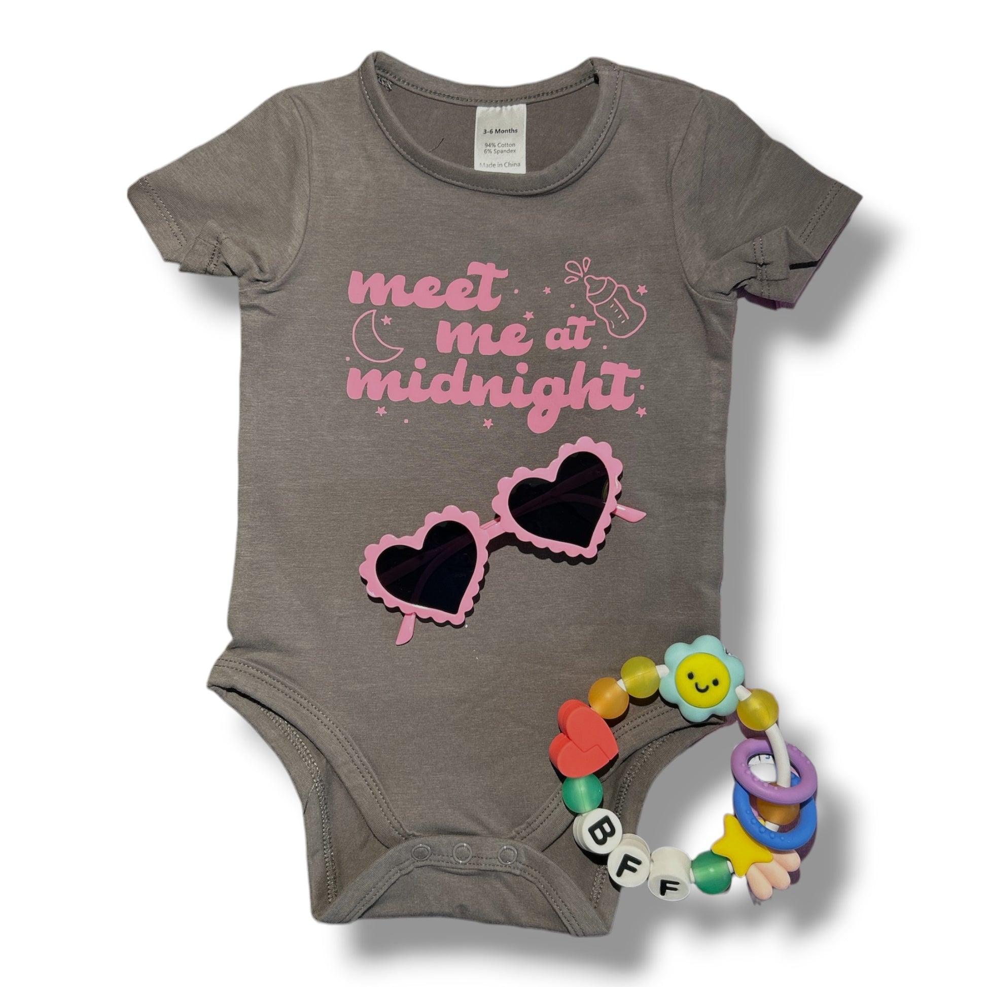 Gray baby onesie with pink sunglasses graphic and text, accompanied by a colorful baby rattle on a white background.