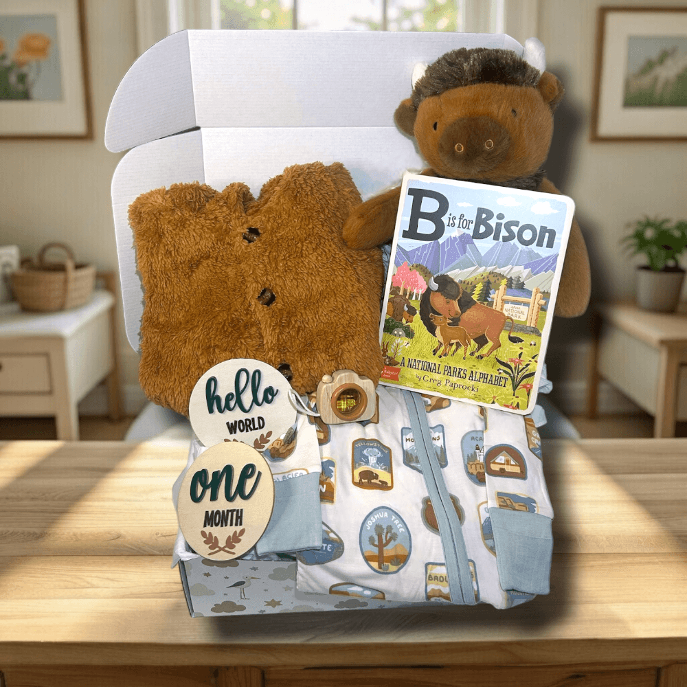 Baby gift set with bison, angel dear pajamas, book, and milestone cards on a wooden surface.
