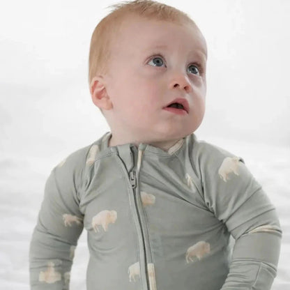 Baby wearing a light gray onesie with animal patterns on a white background