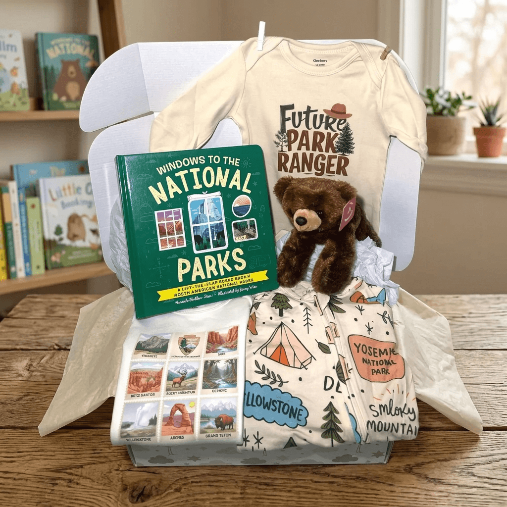 Baby gift set with 'Future Park Ranger' shirt, teddy bear, book, and blanket on a wooden surface.