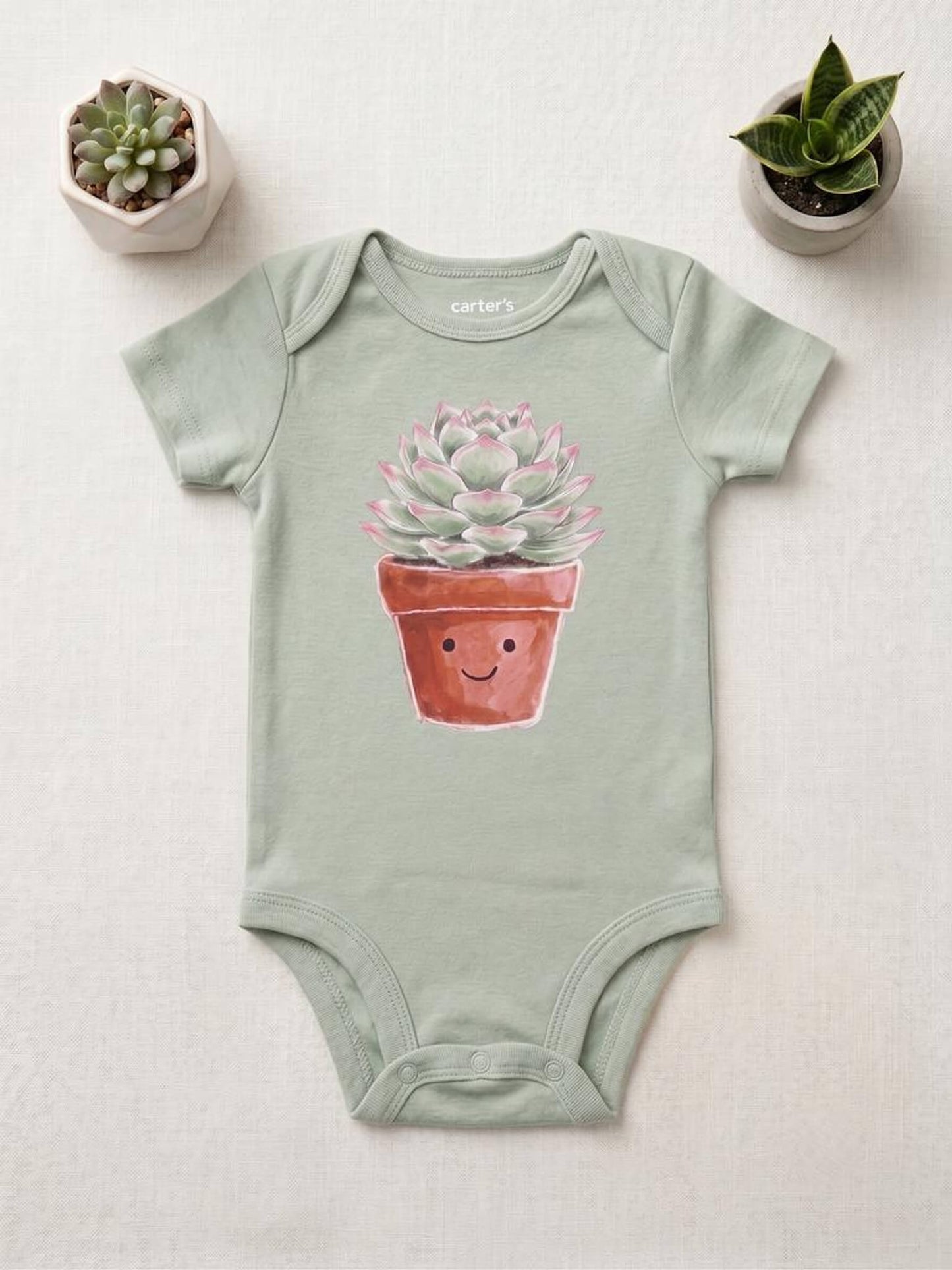 Sage green baby onesie with a potted plant design on a light gray background