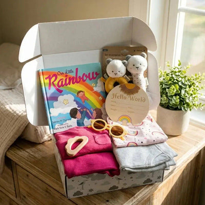 Baby gift box with books, clothes, and toys on a wooden dresser.
