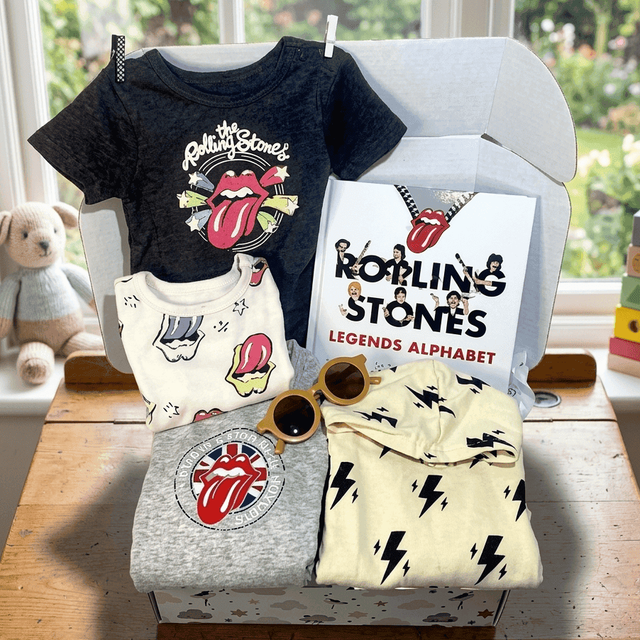Collection of Rolling Stones-themed children's clothing and accessories on a table with a window in the background.