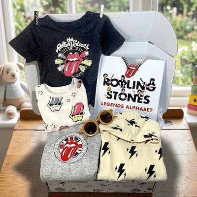 Collection of Rolling Stones-themed children's clothing and accessories on a table with a window in the background.
