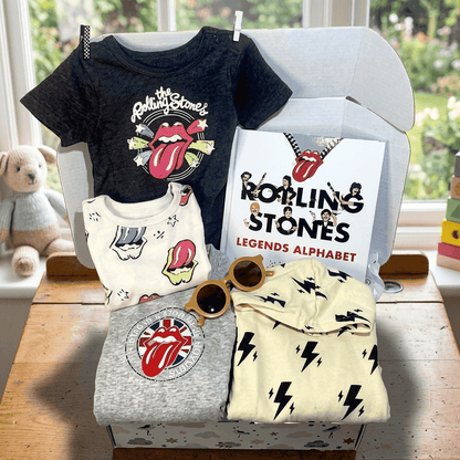 Collection of Rolling Stones-themed children's clothing and accessories on a table with a window in the background.