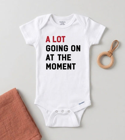 White baby onesie with text and a wooden toy on a light gray background