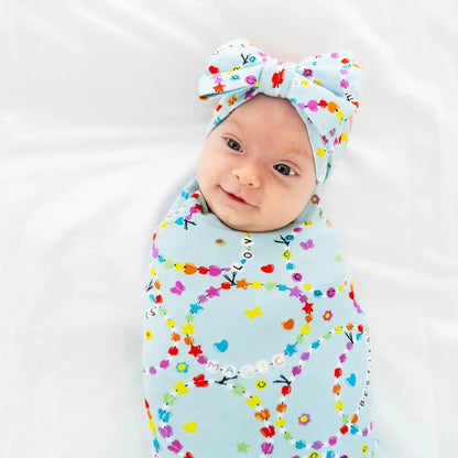 Baby wrapped in a colorful swaddle with a matching headband on a white background