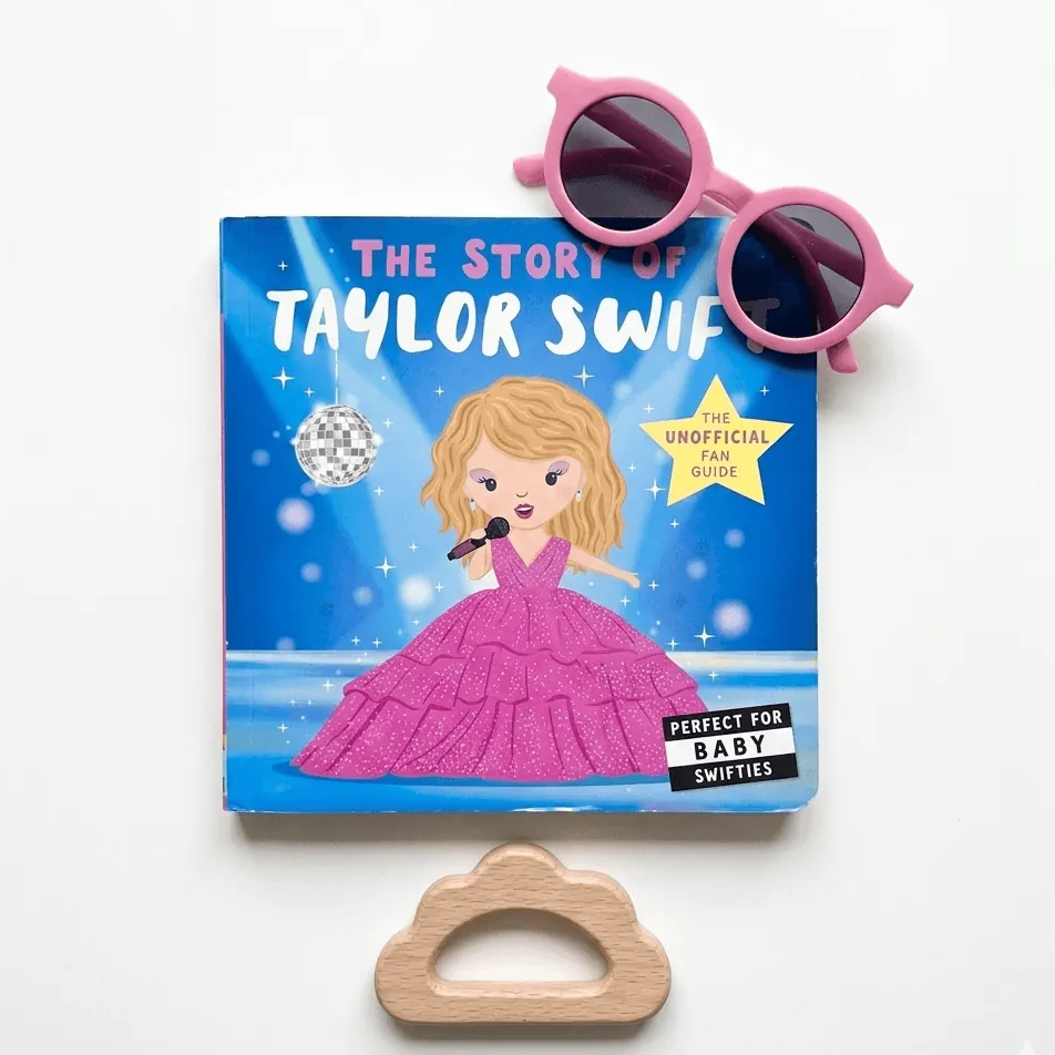 Book titled 'The Story of Taylor Swift' with sunglasses and a wooden cloud-shaped object on a white background