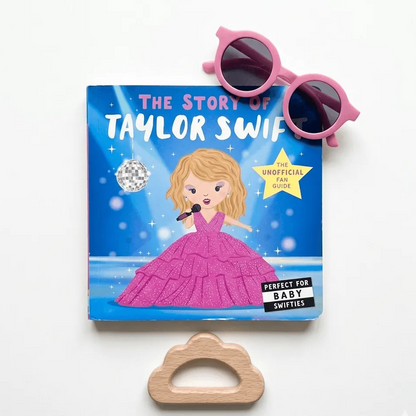 Book titled 'The Story of Taylor Swift' with sunglasses and a wooden cloud-shaped object on a white background