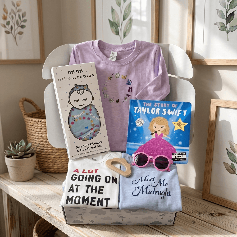 Baby items including t-shirts, a blanket, and books on a wooden surface with a neutral background.