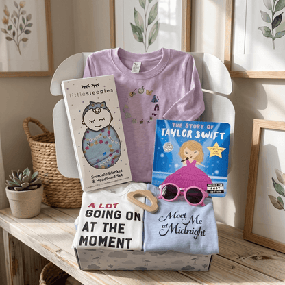 Baby items including t-shirts, a blanket, and books on a wooden surface with a neutral background.