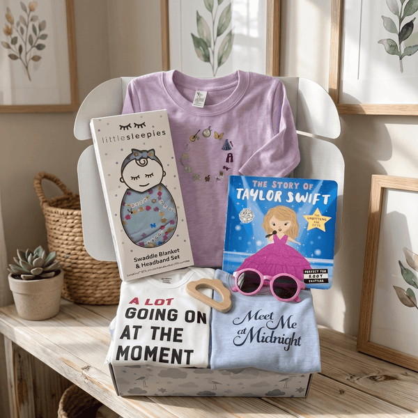 Baby items including t-shirts, a blanket, and books on a wooden surface with a neutral background.
