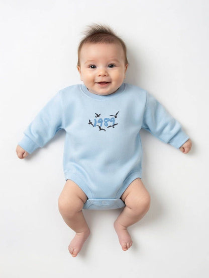 Baby wearing a light blue onesie with a design on a white background