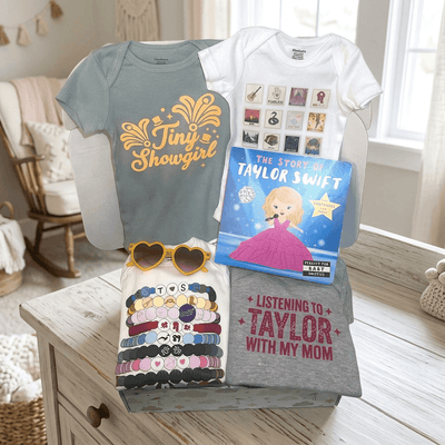 Collection of t-shirts and a book on a wooden surface with a baby chair in the background.