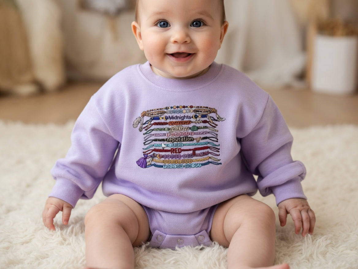 Baby wearing a purple sweatshirt with colorful text design on a fluffy white rug.