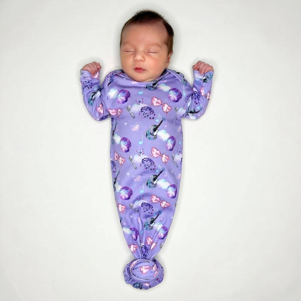 Newborn baby sleeping in a purple swaddle with cartoon designs on a white background