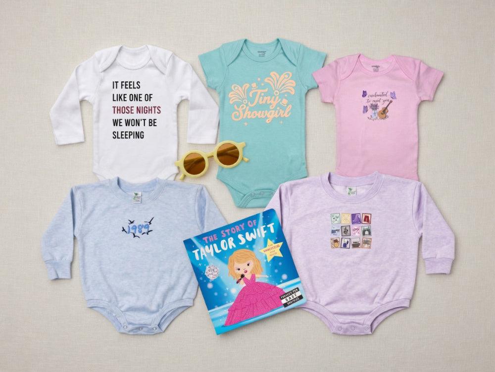 Collection of baby onesies and a book titled 'The Story of Taylor Swift' on a light gray background