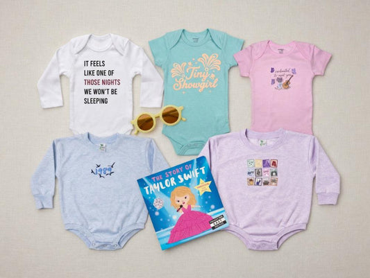 Collection of baby onesies and a book titled 'The Story of Taylor Swift' on a light gray background