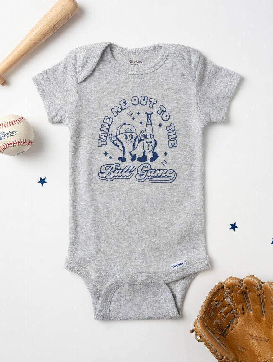 Gray baby onesie with 'Take Me Out to the Ball Game' design, surrounded by baseball-themed items on a white background.