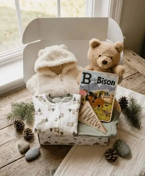 Baby gift set with clothes, a teddy bear, and a book on a wooden surface.