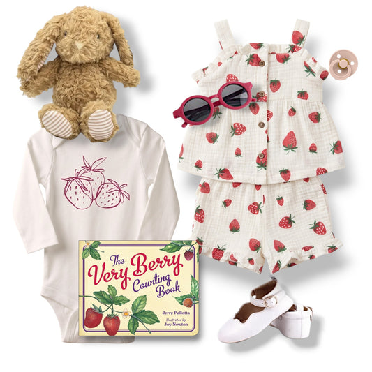 Baby outfit with strawberry-themed dress, onesie, and book, accompanied by a plush toy and pacifier.