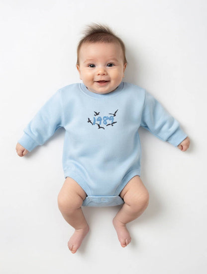 Baby wearing a light blue onesie with a design on a white background